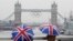 Two tourists stand under Union flag umbrellas as they take pictures from London Bridge, of Tower Bridge adorned with the Olympic rings, on a wet summer's morning in central London July 6, 2012.