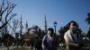 Tourists walk as municipality workers wearing a face mask and protective suits disinfect the area surrounding the historical Sultan Ahmed Mosque, also known as Blue Mosque, amid the coronavirus outbreak, Istanbul, March 21, 2020.