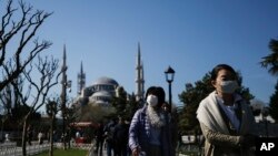 Tourists walk as municipality workers wearing a face mask and protective suits disinfect the area surrounding the historical Sultan Ahmed Mosque, also known as Blue Mosque, amid the coronavirus outbreak, Istanbul, March 21, 2020.