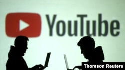 资料图：两位使用移动设备的人士站在YouTube图标投影前