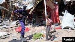 A Somali security officer walks past a child as he secures the scene of an explosion at a market in Wadajir district in Mogadishu, Somalia, Nov. 26, 2018.