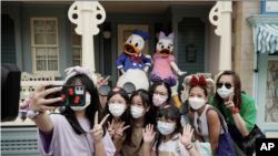 Pengunjung mengenakan masker berfoto bersama Donald Duck dan Daisy Duck di Disneyland Hong Kong, 25 September 2020.