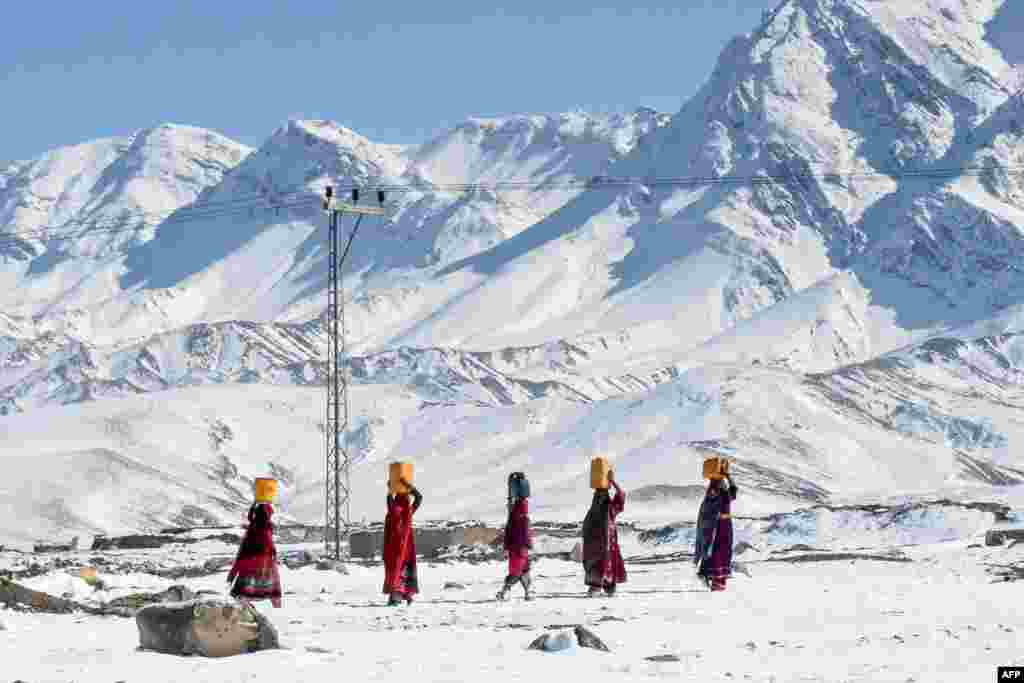 Local residents carry water pots above their heads as they walk back to their homes after heavy snowfall in the Khanozai area, some 75 kilometers northeast of the provincial capital Quetta, Pakistan.