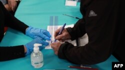 An electoral officer wears gloves as a voter signs on March 15, 2020, in Cucq, France, during the first round of mayoral elections, as the country battles the coronavirus that causes the COVID-19 disease.