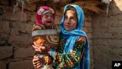 FILE - Qandi Gul, 10, holds her brother outside their home housing those displaced by war and drought near Herat, Afghanistan, Dec. 16, 2021. 