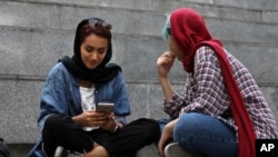 FILE: In this Tuesday, July 2, 2019 photo, an Iranian woman works on her cell phone outside of a shopping mall in northern Tehran, Iran. Before Iranians can check out the latest offerings on Twitter or YouTube, they must search for the best workaround to bypass official censors.