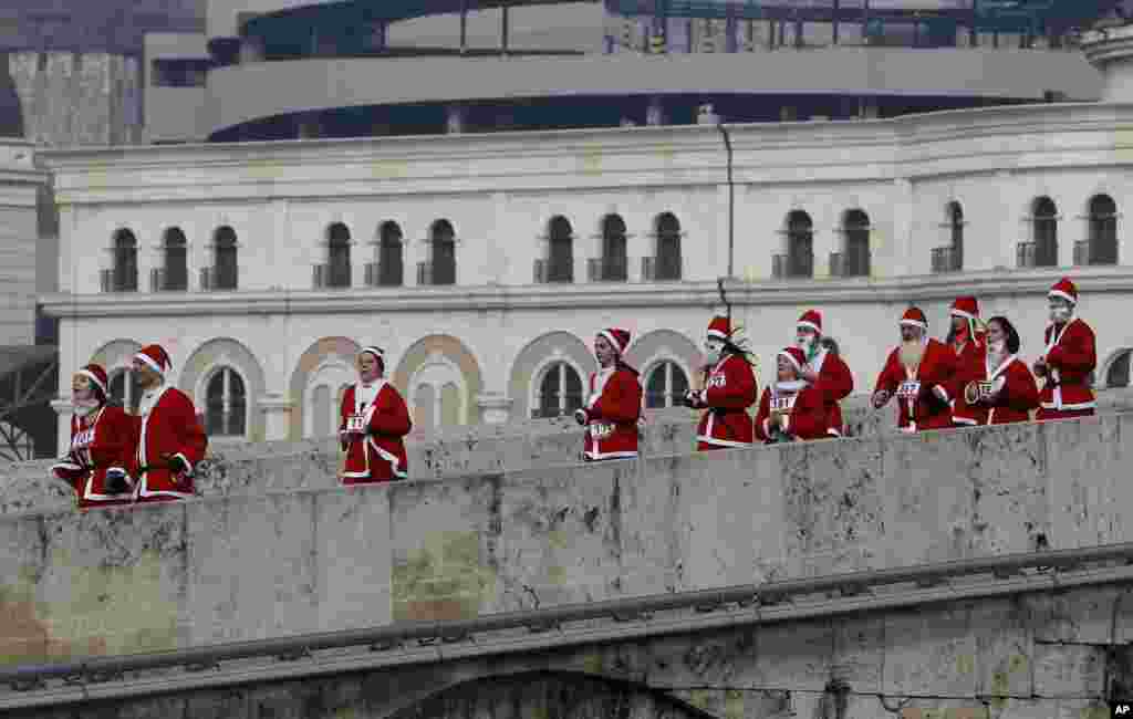 Para peserta lomba lari Sinterklas lari menyeberangi jembatan dengan mengenakakan kostum Sinterklas di ibukota Macedonia, Skopje, 25 Desember 2016.