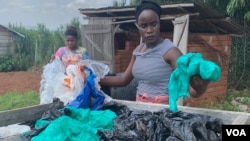 Aweko Faith, right, and Rachel Mema sort through polythene bags for washing, in Mpigi district, Uganda. (H. Athumani/VOA) 