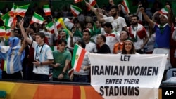 FILE - Fans cheer and wave the flag of Iran as Darya Safai (R) holds a large sign protesting the fact that women have not been allowed to attend volleyball matches in Iran.