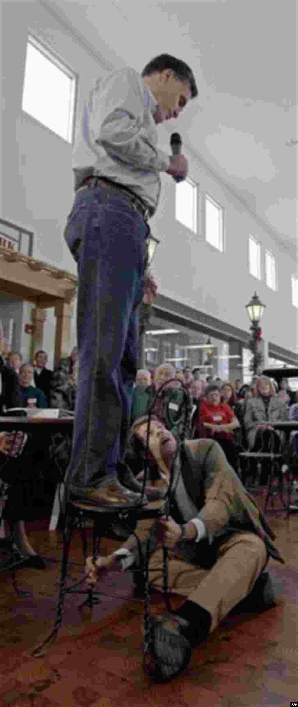 Republican presidential candidate, former Massachusetts Gov. Mitt Romney looks down at an campaign worker holding his chair as he speaks during a campaign stop at the Music Man Square in Mason City, Iowa Thursday, Dec. 29, 2011. (AP Photo/Charlie Riedel)