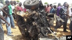 Warga mengerumuni rongsokan mobil yang meledak di lokasi gereja di Yelwa, Bauchi (3/6).