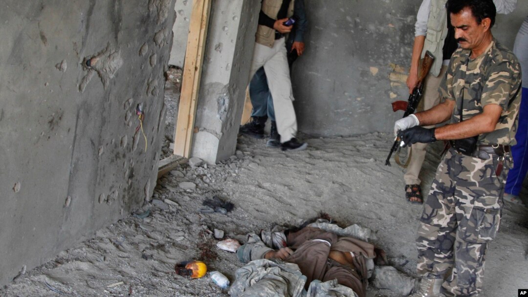 An Afghan security officer stands near the body of an insurgent killed in a battle near Kabul airport, Afghanistan, June, 10, 2013. 
