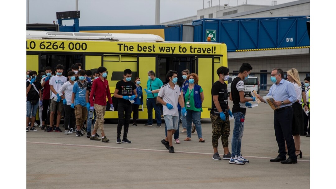 Deputy Migration Minister Giorgos Koumoutsakos, right, greets the 25 unaccompanied refugee children as they prepare to board a plane to Lisbon, Portugal at Athens International Airport, July 7, 2020.