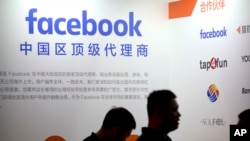 FILE - Visitors walk past the Facebook logo at an exhibitor's display at the Global Mobile Internet Conference (GMIC) in Beijing, April 26, 2018.