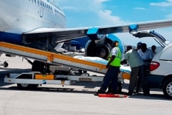 In this photo released by the Bahamas ZNS Network, employees oversee the arrival of the bodies of four women and three men, including billionaire coal entrepreneur Chris Cline and his daughter, at the airport in Nassau, Bahamas, July 5, 2019.