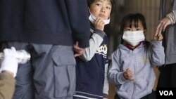 Dua orang anak menyaksikan ayahnya sedang dideteksi oleh petugas apakah terkena radiasi di Fukushima, Jepang (29/3).