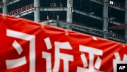 In this April 16, 2017 photo, workers prepare to load cables at a building construction site as a propaganda banner reads "The Party Secretary General Xi Jinping" on display at the Central Business District in Beijing.