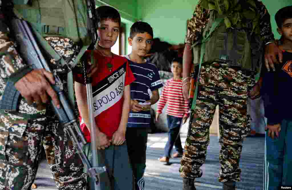 Kashmiri children stand with Indian security personnel inside a polling station, ahead of the second phase of the assembly elections, in Srinagar.