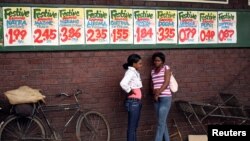 FILE: Women chat near posters advertising food prices outside a shop in Harare, Zimbabwe. (REUTERS/Siphiwe Sibeko - RC199935AA00)