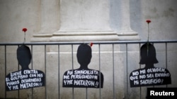 FILE - Cut-out depicting victims of human rights abuse during the rule of former dictator Augusto Pinochet hang on a fence next to the "La Moneda" Presidential Palace during a rally in Santiago, Sept. 11, 2015. 