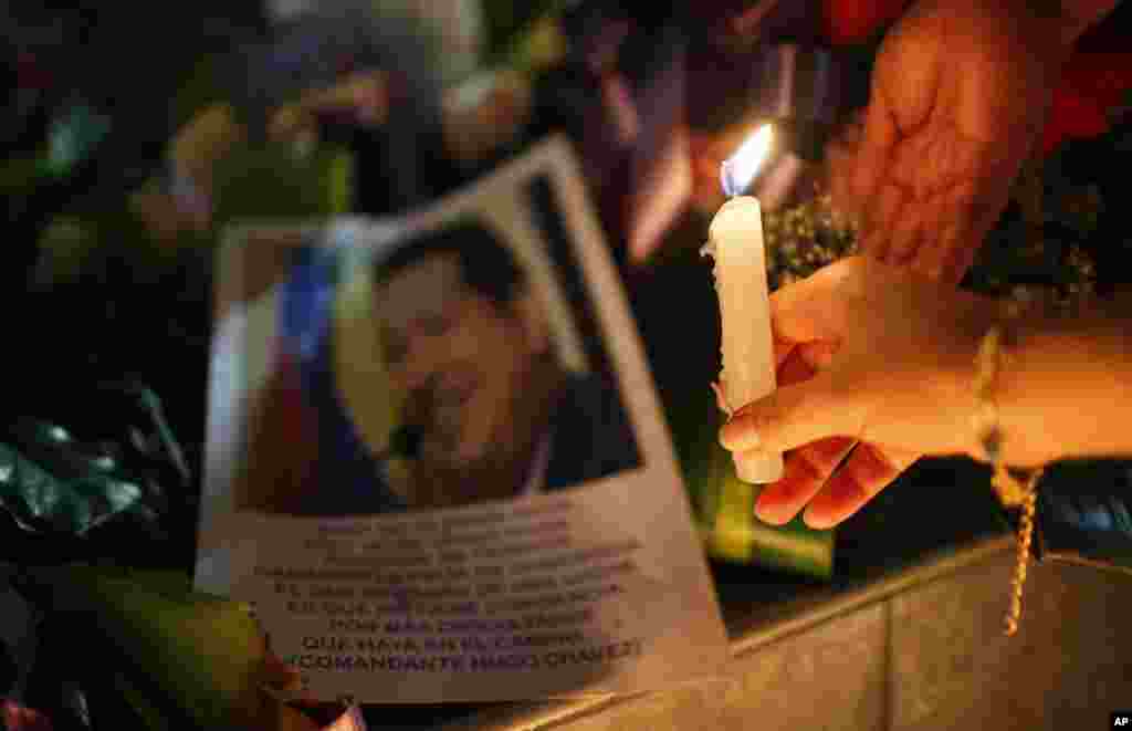 A woman places a candle in front of an image of Venezuelan President Hugo Chavez outside Venezuela's embassy in La Paz, Bolivia, March 5, 2013. 