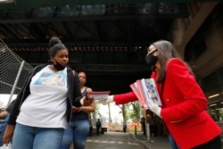 FILE - U.S. Rep. Alexandria Ocasio-Cortez, D-N.Y., right, hands out leaflets explaining how to vote early or by absentee ballot to passers-by at the Parkchester subway station in the Bronx borough of New York, June 15, 2020.