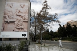 A municipal worker wearing a protective suit sprays disinfectant outside Acropolis museum as the Parthenon temple is seen in the background in Athens on March 24, 2020.