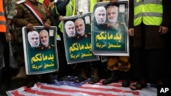 FILE - Yemeni Shiite Houthis stand on a representation of the U.S. flag while holding posters of Abu Mahdi al-Muhandis, left, and Qassem Soleimani during a protest against a U.S. airstrike in Iraq that killed them both, in Sanaa, Yemen, Jan. 6, 2020.