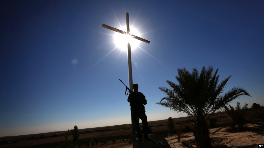 FILE - A member of the Babylon Brigades stands beneath a cross in the town of Khidr Ilyas, southeast of Mosul, Nov. 22, 2016.