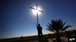 FILE - A member of the Babylon Brigades stands beneath a cross in the town of Khidr Ilyas, southeast of Mosul, Nov. 22, 2016.