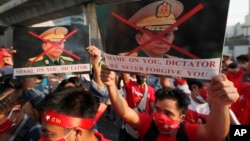 Burmese living in Thailand hold pictures of Myanmar military Commander-in-Chief Senior Gen. Min Aung Hlaing during a protest in front of the Myanmar Embassy, in Bangkok, Thailand, Monday, Feb. 1, 2021. 