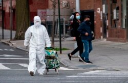 A woman wearing a hazmat suit and googles pulls her grocery cart in the streets in Queens, a borough of New York City amid the coronavirus pandemic on April 20, 2020 in New York City. (Photo by Johannes EISELE / AFP)