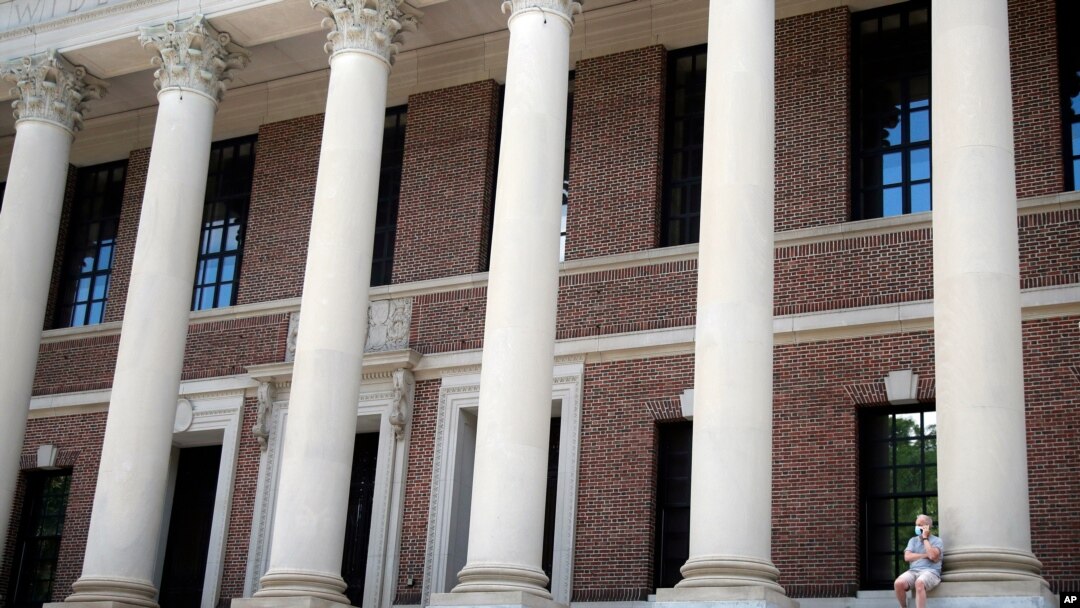FILE - A man wearing a face mask in concern for the coronavirus, talks on his phone, June 26, 2020, on the steps of Harvard University's Widener Library in Cambridge, Mass.