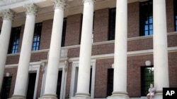 A man wearing a face mask in concern for the coronavirus, talks on his phone, June 26, 2020, on the steps of Harvard University's Widener Library, in Cambridge, Mass.