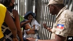 A Haitian police officer asks a woman to move away from a gate at the US Embassy in Port-au-Prince, Haiti, July 9, 2021.