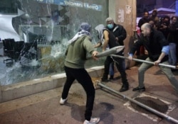 FILE - Anti-government protesters smash a bank widow during ongoing protests against the Lebanese central bank's governor and against the deepening financial crisis, at Hamra trade street, in Beirut, Lebanon, Jan. 14, 2020.