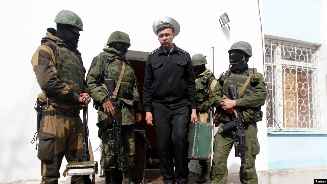 FILE - A Ukrainian naval officer (C) passes by armed men, believed to be Russian servicemen, as he leaves the naval headquarters in Sevastopol, March 19, 2014.