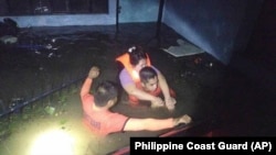 In this photo provided by the Philippine Coast Guard, rescuers help a resident as they navigate floods caused by Tropical Storm Trami in Guinobatan, Albay province, Philippines, Oct. 22, 2024.