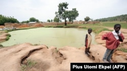 (FILE) Two young boys stand in front of a pond infected with lead poison at Dareta village, Anka district in Zamfara State on June 10, 2010. 