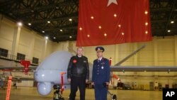 Turkey's President Recep Tayyip Erdogan poses for a photo with a Turkish army commander in front of a drone at a military airbase in Batman, Turkey, Saturday, Feb. 3, 2018.