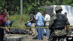 A Mexican Navy soldier watches as forensic workers remove a body and dig for others at a clandestine site that was found in the town of Tuncingo, Mexico, 03 Nov 2010