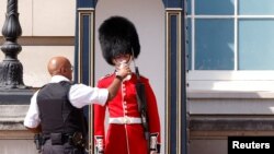 Seorang anggota Pengawal Ratu di luar Istana Buckingham, menerima air minum dari petugas, saat cuaca panas melanda London, Inggris, 18 Juli 2022. (REUTERS/John Sibley )