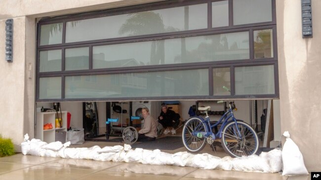 Fitness trainer Kelly Curtis, right, works out at her studio protected with sandbags in preparation for a storm along the Peninsula in Long Beach, Calif., Feb. 19, 2024.