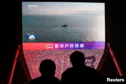 Orang-orang melihat layar yang menayangkan cuplikan berita latihan militer yang dilakukan di Selat Taiwan oleh PLA, di Beijing, 14 Oktober 2024. (Foto: Reuters)