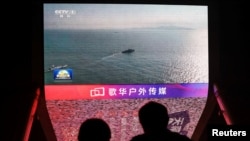 People look at a screen showing news footage of military drills conducted in the Taiwan Strait by the PLA, in Beijing, October 14, 2024.