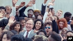 FILE - U.S. President George H.W. Bush is surrounded by cheering students from the Independent Living Program in Los Angeles, as Bush prepared to leave Los Angeles International Airport after presenting a Point of Light award in the area, May 21, 1990. 