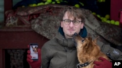 Vaidas Gecevicius, yang mengembangkan aplikasi pengadopsian anjing tak bertuan berpose dengan seekkor anjing dan menunjukkan profile sang anjing dalam sebuah aplikasi GetPet, 2 Februari 2019, Vilnius, Lithuania (foto: AP Photo/Mindaugas Kulbis)