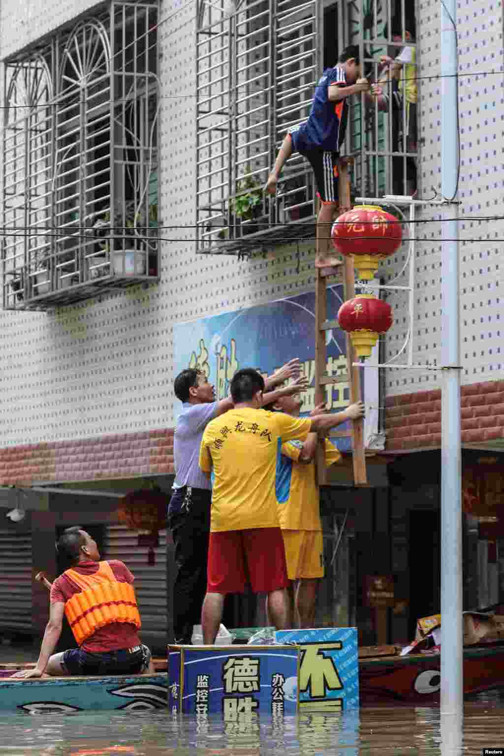 2018年9月1日，中国广东省汕头市一个村庄遭遇暴雨，路上行舟，救援人员架起梯子，一名儿童从楼上爬下来。