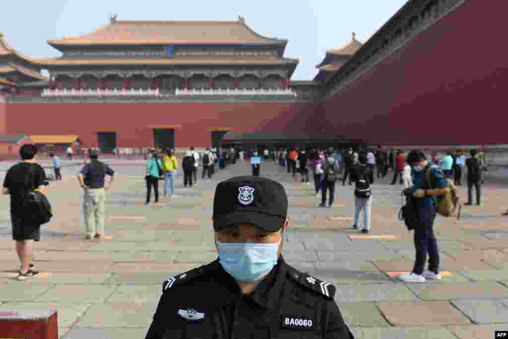 A security guard stands watch as people line up while ensuring social distancing, to enter the Forbidden City, the former palace of China's emperors, in Beijing. The area was reopened three months after it closed due to the coronavirus crisis.