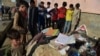 FILE - Onlookers stand next to the backpacks and books of victims the day after multiple blasts outside a girls' school in Dasht-e-Barchi on the outskirts of Kabul, May 9, 2021.